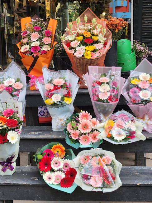 A selection of flower bouquets arranged on a wooden outdoor display, featuring a variety of fresh blooms including pink and white gerbera daisies, vibrant red and yellow chrysanthemums, and pink carna